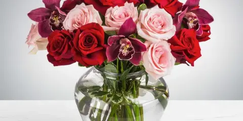 A floral arrangement featuring red and pink roses and purple orchids in a clear glass vase.