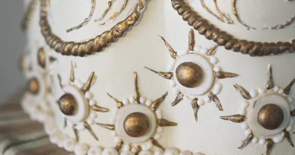 Close-up of a white wedding cake decorated with gold leaf sunburst motifs and piped borders.