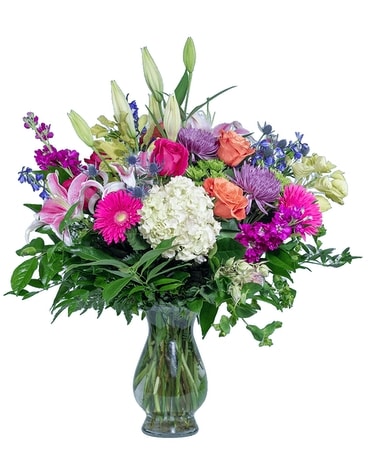 A colorful floral arrangement featuring lilies, roses, and chrysanthemums in a clear glass vase.
