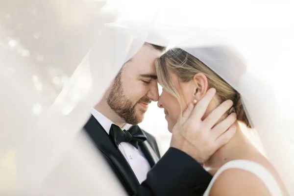 Close-up portrait of a bride and groom in wedding attire, with the groom holding the bride's face under her veil.