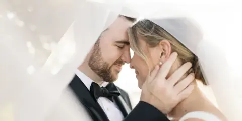 Close-up portrait of a bride and groom in wedding attire, with the groom holding the bride's face under her veil.