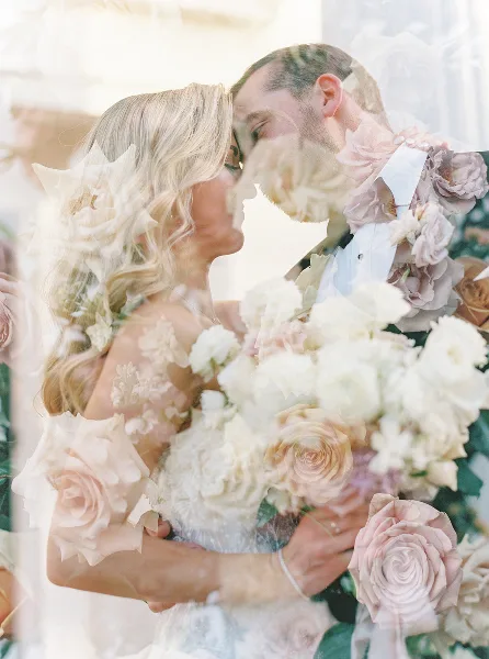 A bride and groom sharing a moment, with the bride holding a large, romantic bouquet of white and blush roses.
