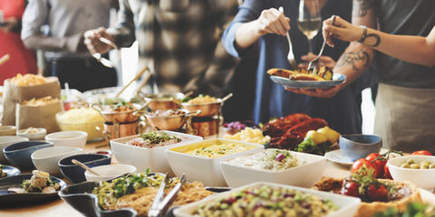 A buffet table filled with various prepared dishes and salads, with people serving themselves plates of food.