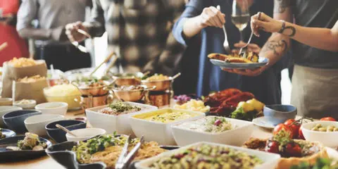 A buffet table filled with various prepared dishes and salads, with people serving themselves plates of food.
