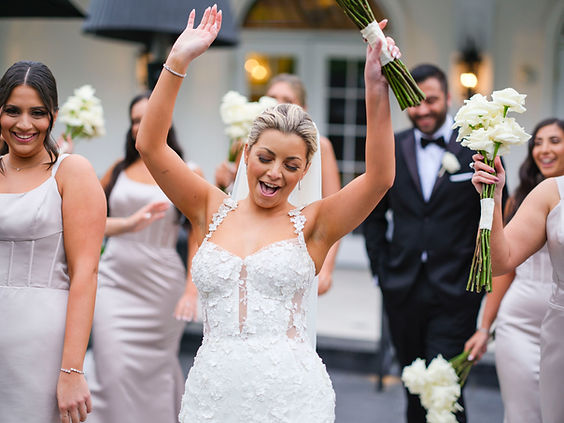 Bride cheers while holding her bouquet in the air as bridesmaids walk behind her