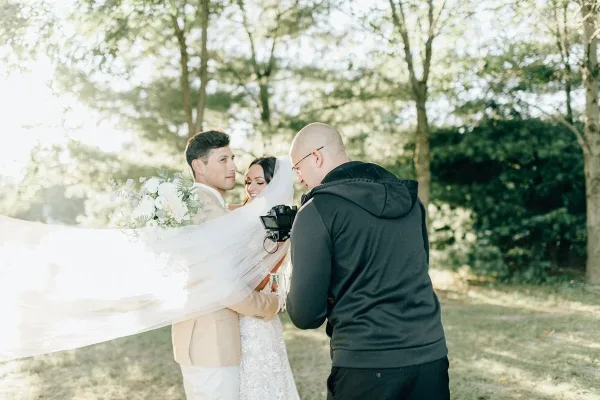 A videographer filming a bride and groom in an outdoor setting.