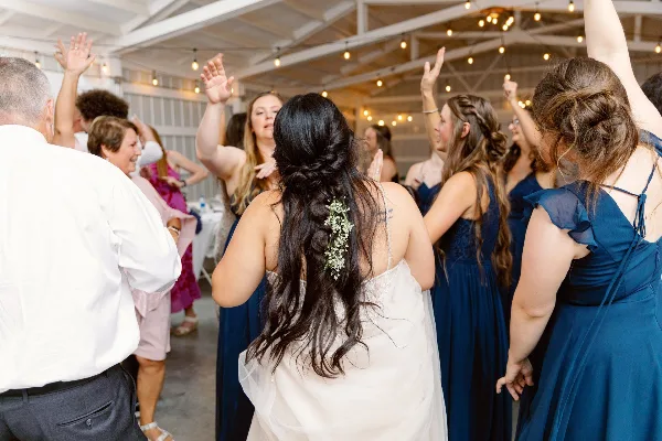 A bride and wedding guests dancing at a reception under string lights.
