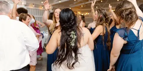 A bride and wedding guests dancing at a reception under string lights.