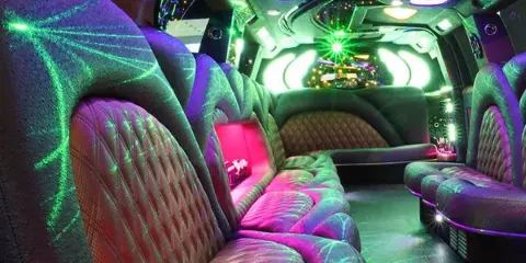 Interior of a party bus featuring plush wraparound seating and vibrant green and purple lighting.