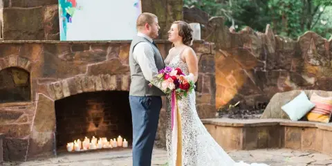 A bride and groom standing in front of a rustic stone fireplace at a wedding venue