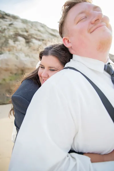 A professional outdoor portrait of a couple, with the woman resting her head on the man's shoulder, both dressed in formal wear.
