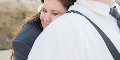A professional outdoor portrait of a couple, with the woman resting her head on the man's shoulder, both dressed in formal wear.