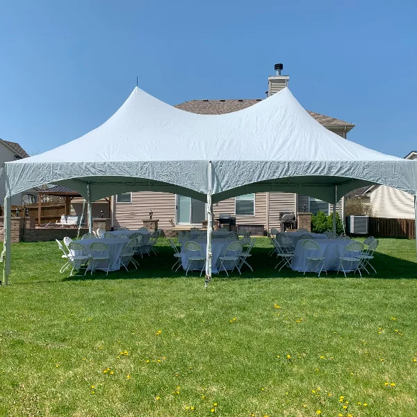 A white event tent set up in a residential backyard with round tables and chairs arranged underneath.