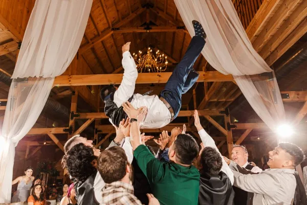 Wedding guests lifting a celebrant beneath draped reception decor
