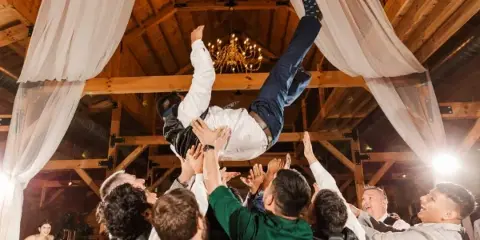 Wedding guests lifting a celebrant beneath draped reception decor