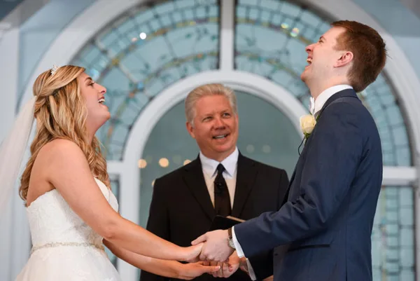 A bride and groom holding hands during a wedding ceremony with an officiant standing behind them.