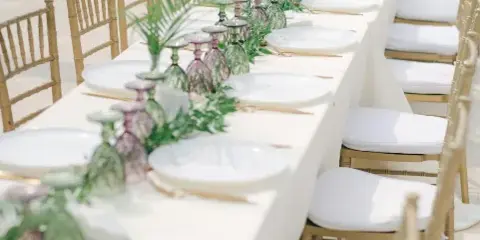 A long reception table set with white linens, gold Chiavari chairs, and a floral centerpiece.