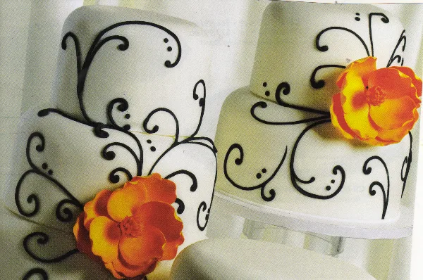 A white multi-tiered wedding cake decorated with black scrollwork and orange flowers.
