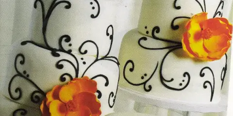 A white multi-tiered wedding cake decorated with black scrollwork and orange flowers.