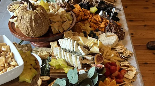 A large, elaborately arranged catering board featuring various cheeses, crackers, dried fruits, and a decorative pumpkin centerpiece.