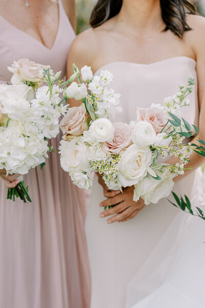 Close-up of a bride and bridesmaid holding white and blush pink floral bouquets.