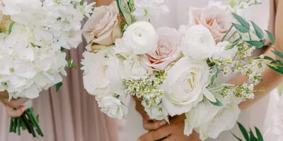 Close-up of a bride and bridesmaid holding white and blush pink floral bouquets.