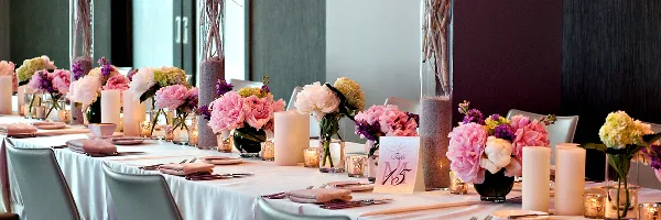 A long wedding reception table decorated with pink and white floral centerpieces, candles, and tableware.