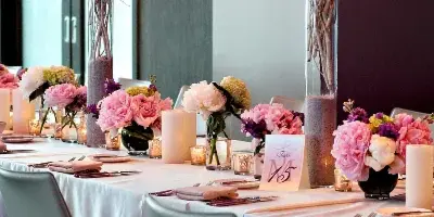 A long wedding reception table decorated with pink and white floral centerpieces, candles, and tableware.