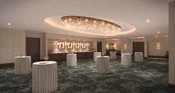 A spacious event ballroom featuring a large circular chandelier and multiple white-draped high-top tables.