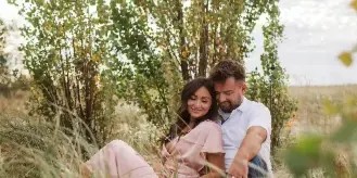 A couple sitting together in a grassy field with trees in the background, overlaid with the text 'Life, Unscripted.'