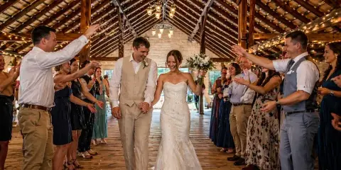 Bride and groom walking through cheering guests in The RED House barn