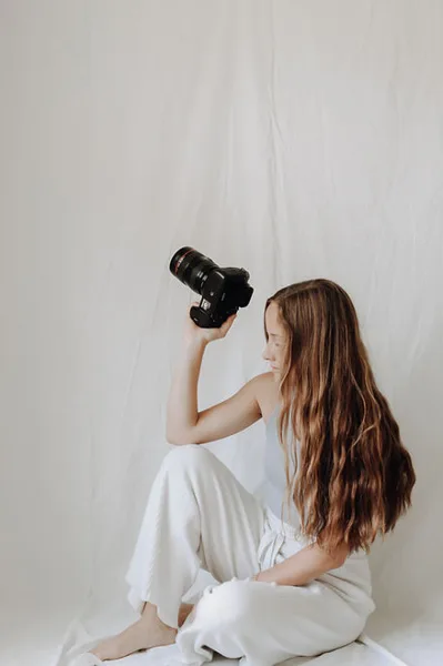 A woman sitting on a white backdrop holding a professional camera
