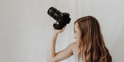 A woman sitting on a white backdrop holding a professional camera