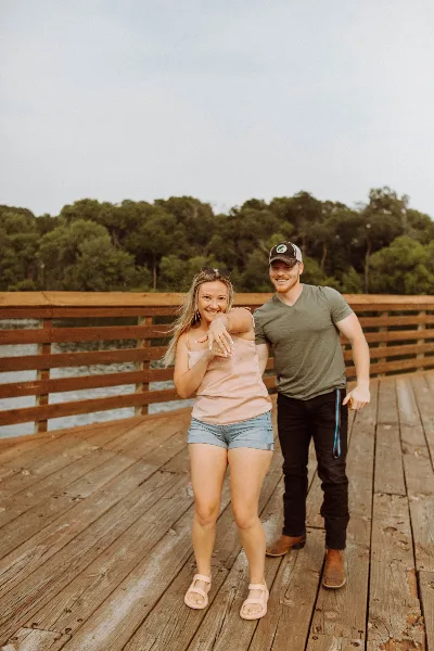 A couple posing for a portrait on a wooden pier near a body of water.