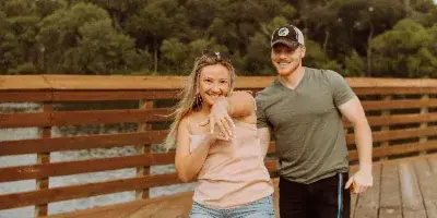 A couple posing for a portrait on a wooden pier near a body of water.