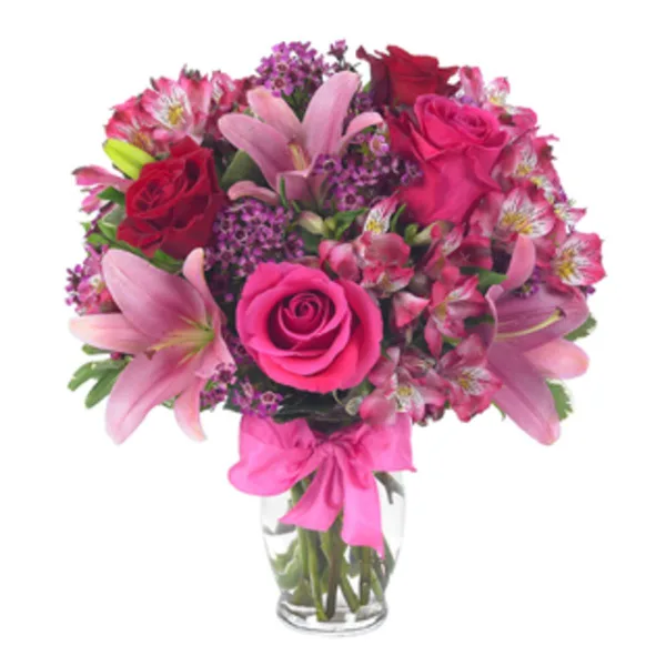 A floral arrangement featuring pink lilies, red roses, and alstroemeria in a clear glass vase.