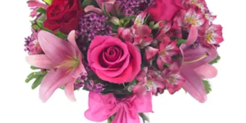 A floral arrangement featuring pink lilies, red roses, and alstroemeria in a clear glass vase.