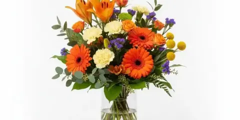 A mixed flower bouquet with orange lilies, gerbera daisies, and carnations in a clear glass vase.