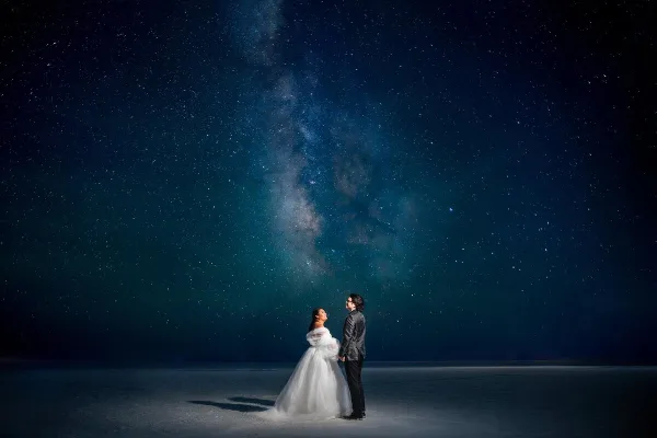A bride and groom standing together under a starry night sky with the Milky Way visible above them.