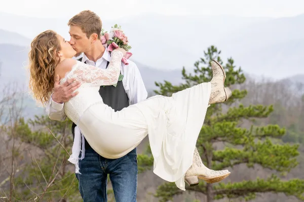 A bride and groom sharing a kiss outdoors with a mountain landscape in the background.