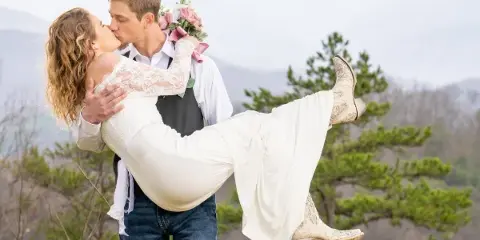 A bride and groom sharing a kiss outdoors with a mountain landscape in the background.