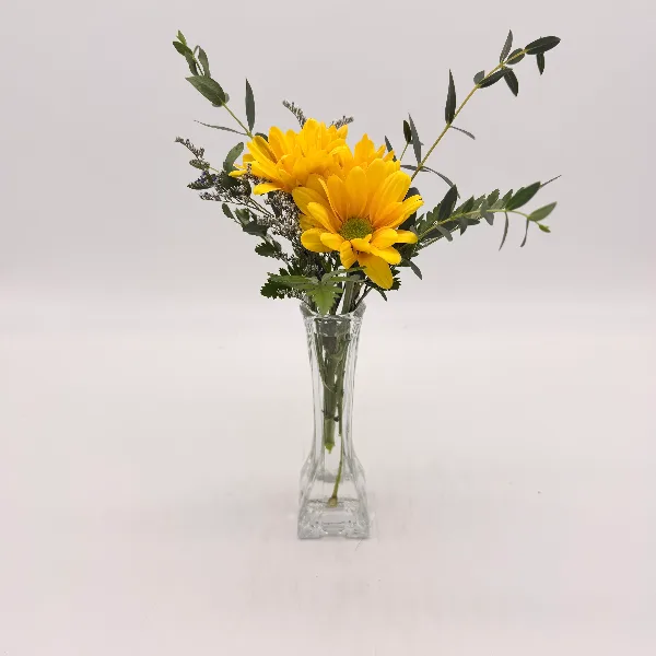 A yellow flower bouquet with greenery in a clear glass vase