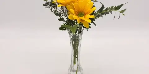 A yellow flower bouquet with greenery in a clear glass vase