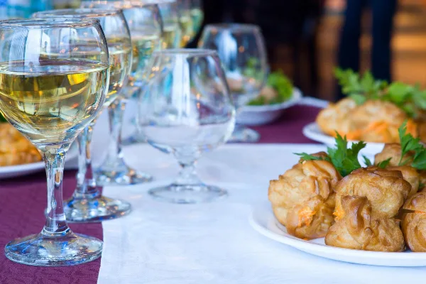 A catering table setting featuring wine glasses and a plate of golden puff pastry appetizers garnished with parsley.