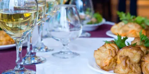 A catering table setting featuring wine glasses and a plate of golden puff pastry appetizers garnished with parsley.