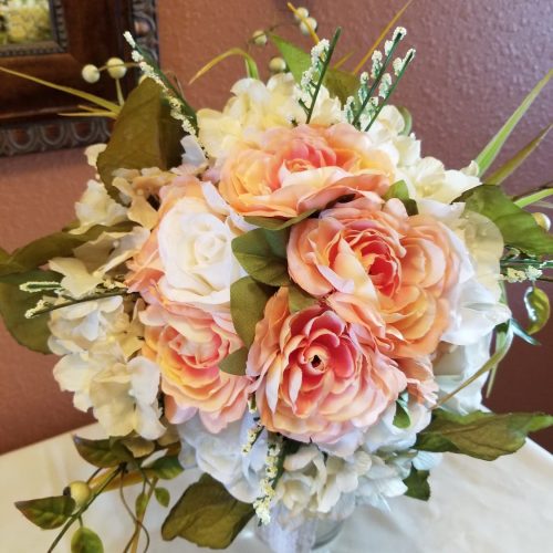 A close-up of a wedding floral arrangement featuring peach and white roses and hydrangeas with greenery.