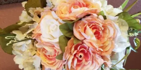 A close-up of a wedding floral arrangement featuring peach and white roses and hydrangeas with greenery.