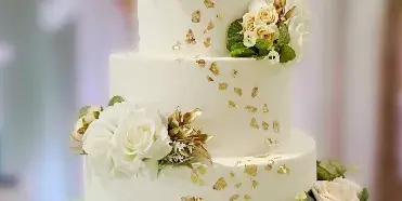 A four-tier wedding cake featuring white and mint green tiers, adorned with white roses, greenery, and gold leaf accents.