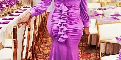 A woman in a purple dress standing in a banquet hall decorated with purple floral arrangements and white table settings.