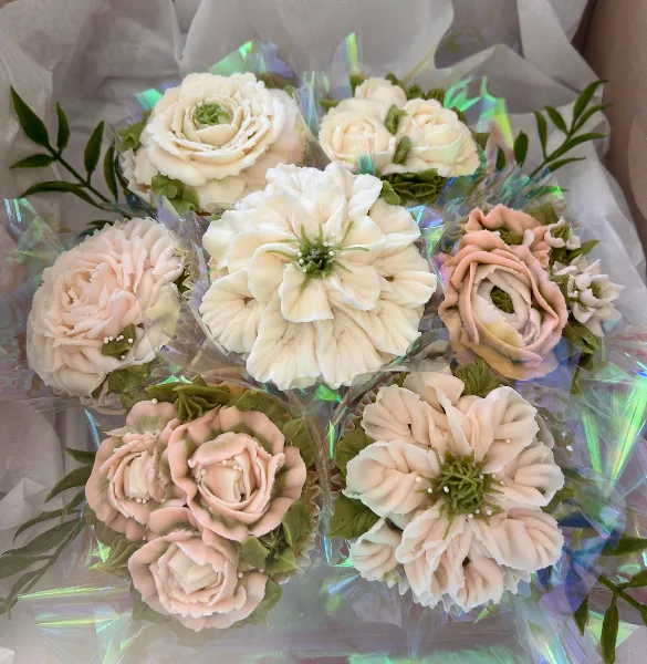 A bouquet of cupcakes decorated with intricate white and pink buttercream flowers and green leaves.